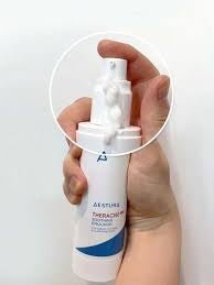 A hand holding a white skincare pump bottle with a blue accent, featuring a circular zoom-in overlay of the white cream being dispensed from the pump.